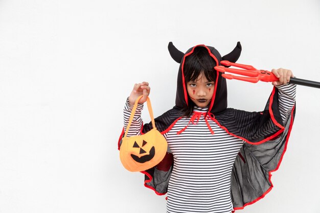 Niña asiática en traje de demonio con tridente negro y rojo, concepto de feliz halloween