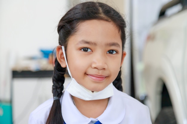 Niña asiática en uniforme de estudiante tailandés con máscara protectora contra la gripe de virus