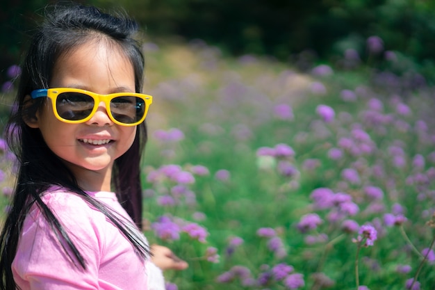 Niña asiática en vestido rosa con gafas de sol de pie en el jardín de flores de color púrpura