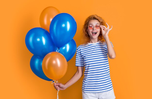 Niña asombrada con globo de cumpleaños en gafas de sol niña feliz de cumplaños sostiene globos de fiesta en el estudio niña con globo para fiesta de cumpleañas aislada sobre fondo amarillo