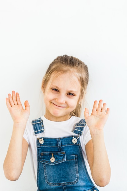 Una niña de aspecto europeo con cabello largo y claro se lleva las manos a la cara, sonríe, las emociones de los niños, la infancia, la escuela