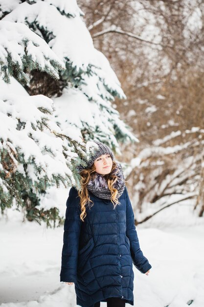 Una niña de aspecto europeo camina en el parque, bosque, invierno y nieve, vestida con ropa de abrigo, gorro, chaqueta, bufanda, descanso, senderismo