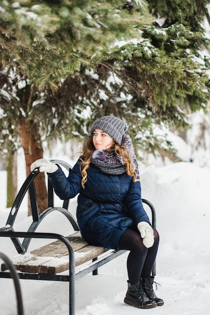 Una niña de aspecto europeo camina en el parque, bosque, invierno y nieve, vestida con ropa de abrigo, gorro, chaqueta, bufanda, descanso, senderismo