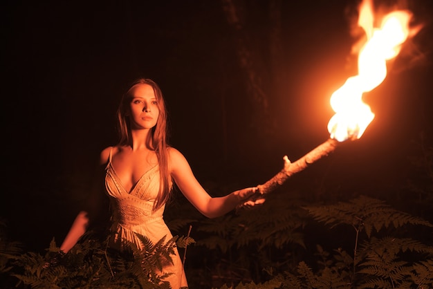 Niña asustada en un bosque oscuro con una antorcha.