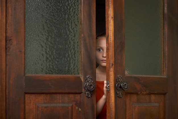 Una niña asustada está mirando por la rendija de la puerta.