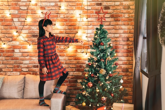 niña atractiva sosteniendo una bola de oro en la sala de estar. linda niña decorando el árbol de navidad en casa. Se acerca el año nuevo y la Navidad.