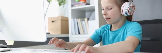 Niña en auriculares escribiendo en el teclado de la computadora en casa