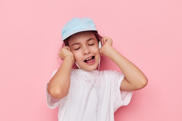 Niña en auriculares posando sobre un fondo rosa