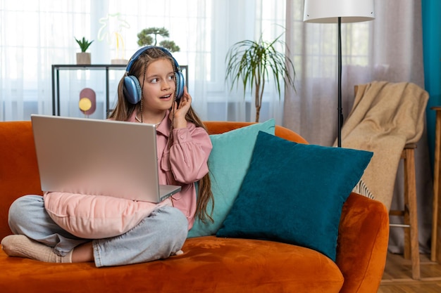 Niña con auriculares que usa una computadora portátil escucha música o aprende a distancia en casa