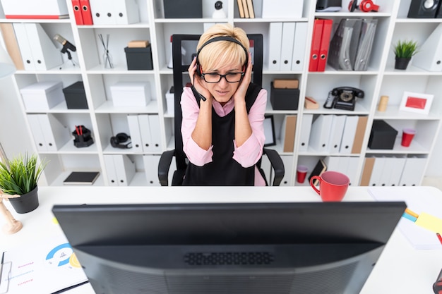 Una niña con auriculares sentado en la mesa de la computadora y cogidos de la mano sobre su cabeza.