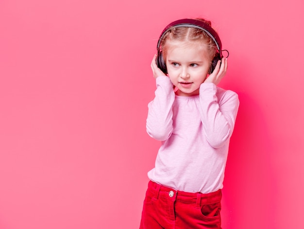 Niña en auriculares sobre fondo rosa