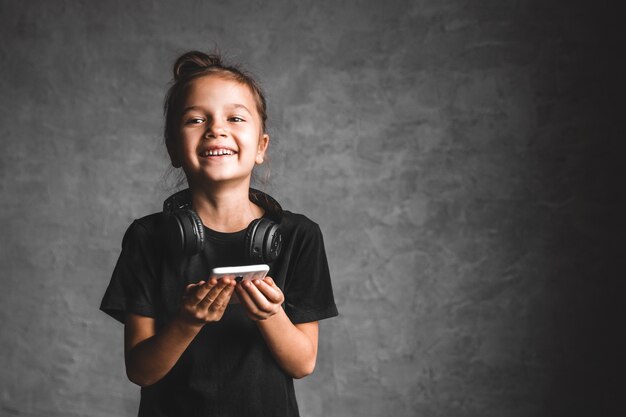 Niña con auriculares y teléfono en una pared gris