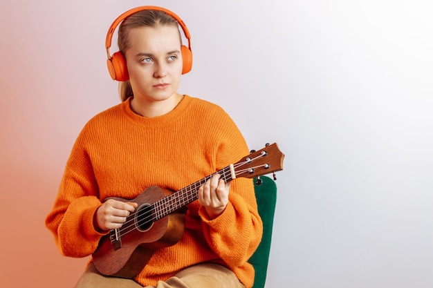 Una niña con auriculares toca el ukelele.