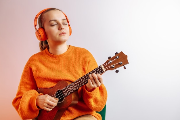 Una niña con auriculares toca el ukelele.