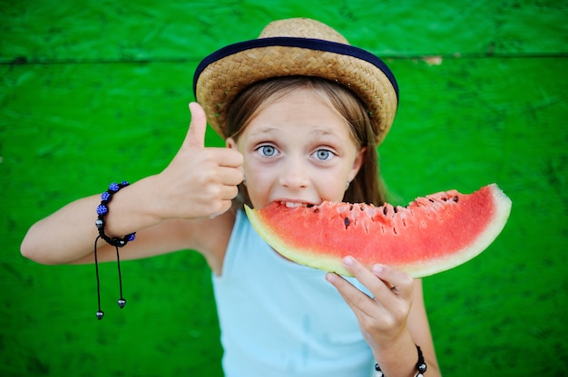 Niña avariciosamente comiendo sandía madura sobre un fondo verde