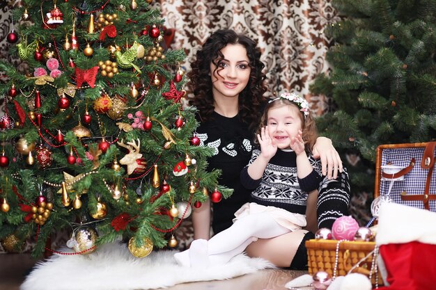 Una niña ayuda a su madre a decorar el árbol de Navidad familiar Vacaciones familiares de invierno y concepto de personas madre feliz e hija pequeña en casa