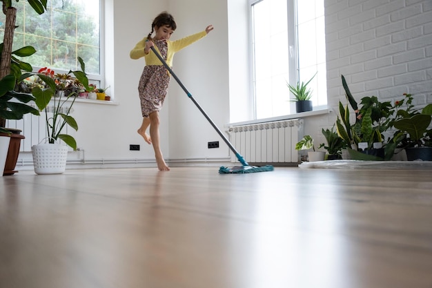 Una niña baila con un trapeador para limpiar el piso en una casa nueva limpieza general en una habitación vacía la alegría de moverse ayuda con las tareas domésticas