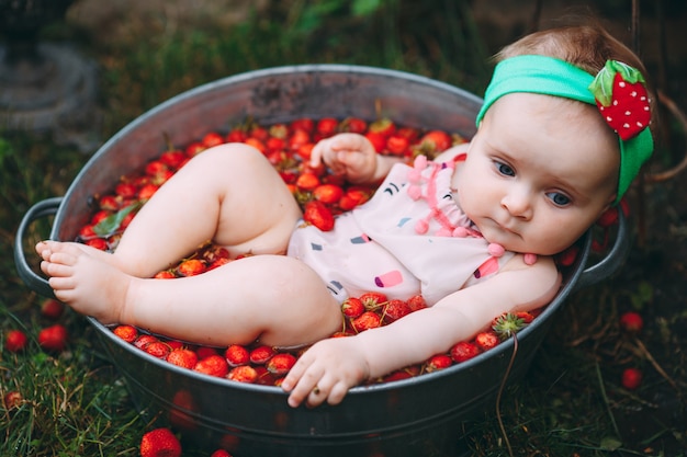 Una niña se baña en una cuenca con fresas en el jardín.