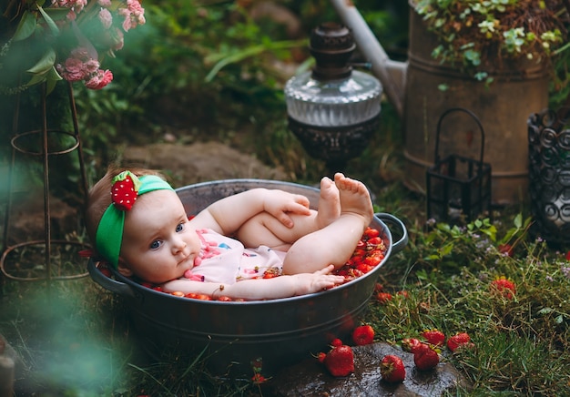 Una niña se baña en una cuenca con fresas en el jardín.