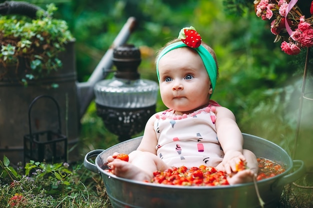 Una niña se baña en un lavabo con fresas en el jardín.