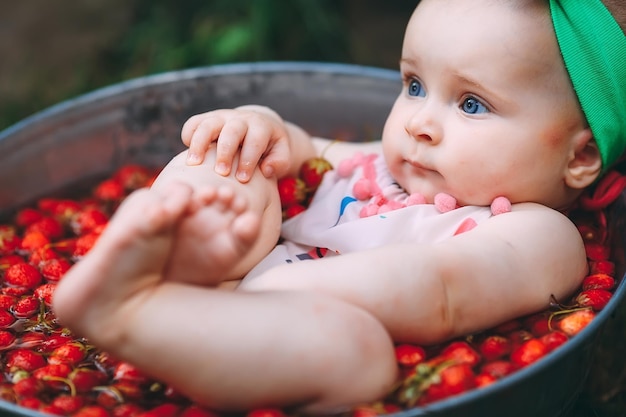 Una niña se baña en un lavabo con fresas en el jardín.