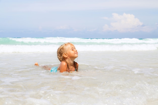 Niña se baña en el mar en la playa con arena blanca