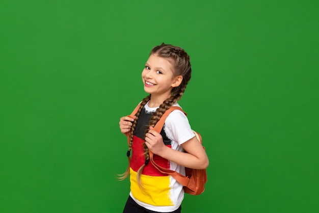 Una niña con una bandera alemana en su camiseta sostiene una cartera a la espalda y sonríe ampliamente Cursos educativos de alemán para escolares