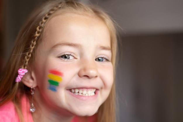 Una niña con una bandera del arcoíris pintada en las mejillas Día del orgullo LGBT Familia Día del niño