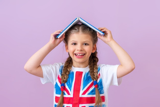 Una niña con una bandera inglesa en su camiseta sostiene un libro sobre su cabeza.