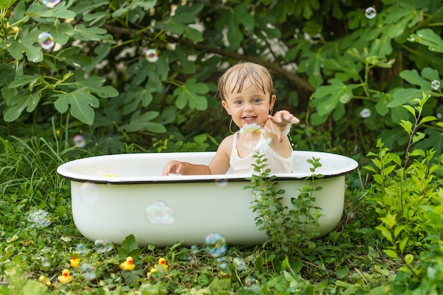 Una niña en un baño retro se baña en la naturaleza y se ríe.