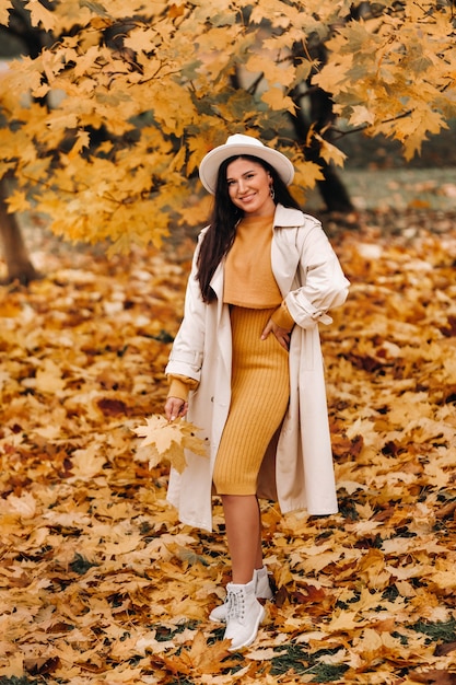 Una niña con una bata blanca y un sombrero sonríe en un parque de otoño