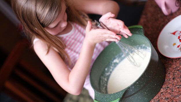 Niña bate los ingredientes para la masa en un tazón con batidor futuro chef y juegos para niños en