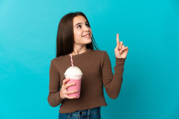 Niña con batido de fresa aislado sobre fondo azul apuntando hacia una gran idea