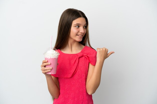 Niña con batido de fresa sobre fondo blanco aislado apuntando hacia el lado para presentar un producto