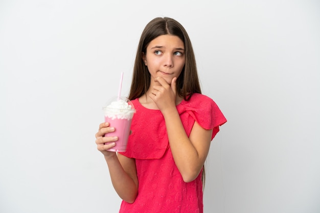 Niña con batido de fresa sobre superficie blanca aislada teniendo dudas y pensando