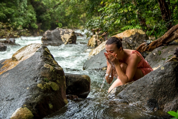 la niña bebe agua de un arroyo de montaña