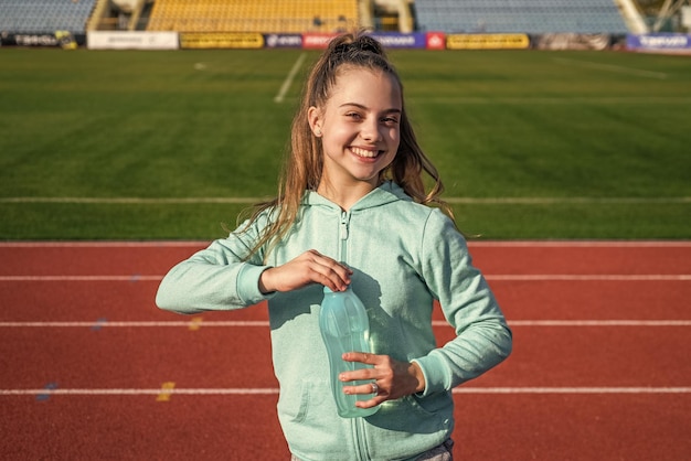 Niña bebe agua después del deporte afuera en la hidratación de la arena del estadio