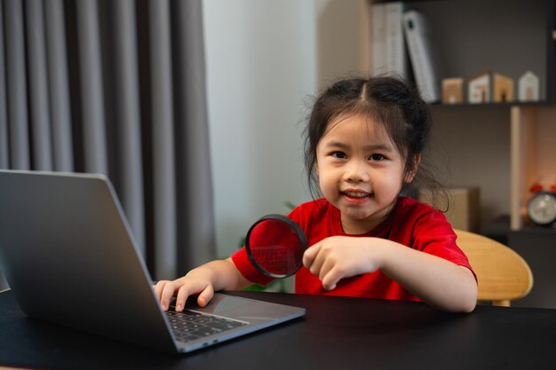 Niña bebé asiática sosteniendo lupa y usando portátil educación para obtener buenas ideas niños y concepto de escuela feliz sonriente estudiante niña aprendiendo estudiando concepto de desarrollo educativo