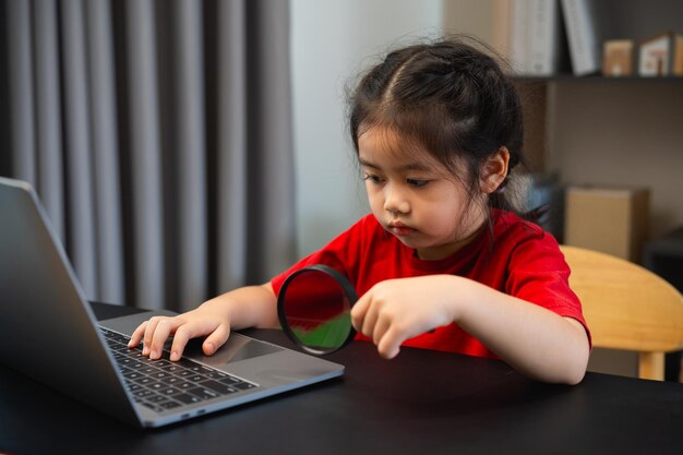 Niña bebé asiática sosteniendo lupa y usando portátil educación para obtener buenas ideas niños y concepto de escuela feliz sonriente estudiante niña aprendiendo estudiando concepto de desarrollo educativo