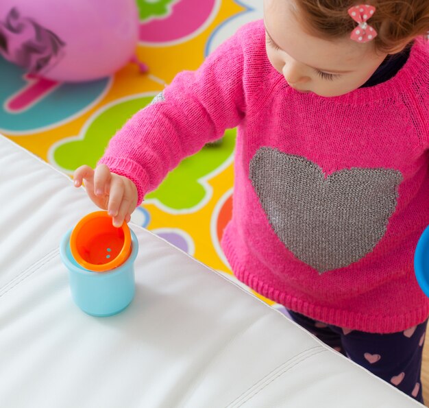 Niña bebé juega con tazas de colores