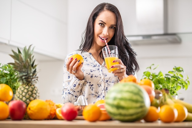 Niña bebe un jugo de naranja recién exprimido con una pajita de papel rodeada de una variedad de frutas.