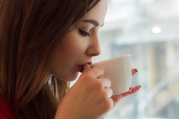 Foto niña bebe té de la taza pequeña en un café con ventana grande