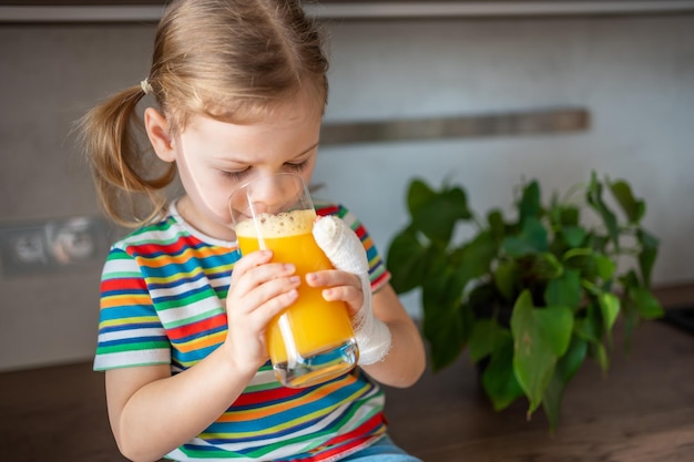 Niña bebiendo jugo fresco sentado en la mesa en la cocina de casa