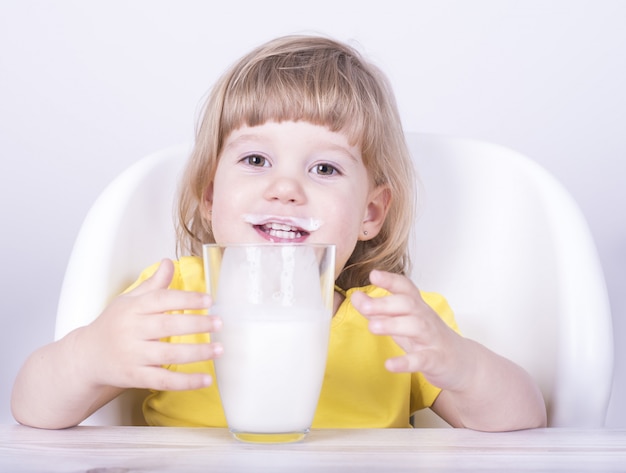 Niña bebiendo un vaso de leche en casa con bigote de leche