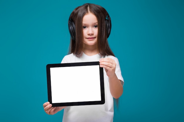 Niña de belleza en camiseta y auriculares con tableta de retención de pelo largo