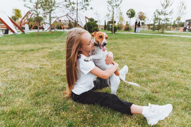 Foto una niña besa y abraza a su perro jack russell terrier en el parque amor entre el dueño y el perro un niño sostiene a un perro en sus brazos
