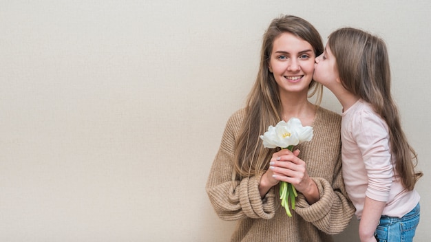 Niña besando a la madre con tulipanes en la mejilla