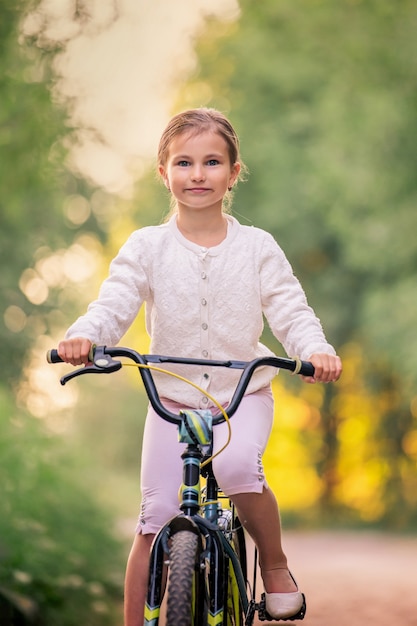 Niña va con una bicicleta por un camino rural en la naturaleza al atardecer