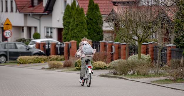 Niña en bicicleta entre casas privadas en Europa durante la primavera vista desde atrás