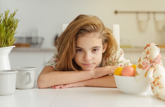 Niña blanca europea de 10 años en la cocina en la mesa con huevos de Pascua